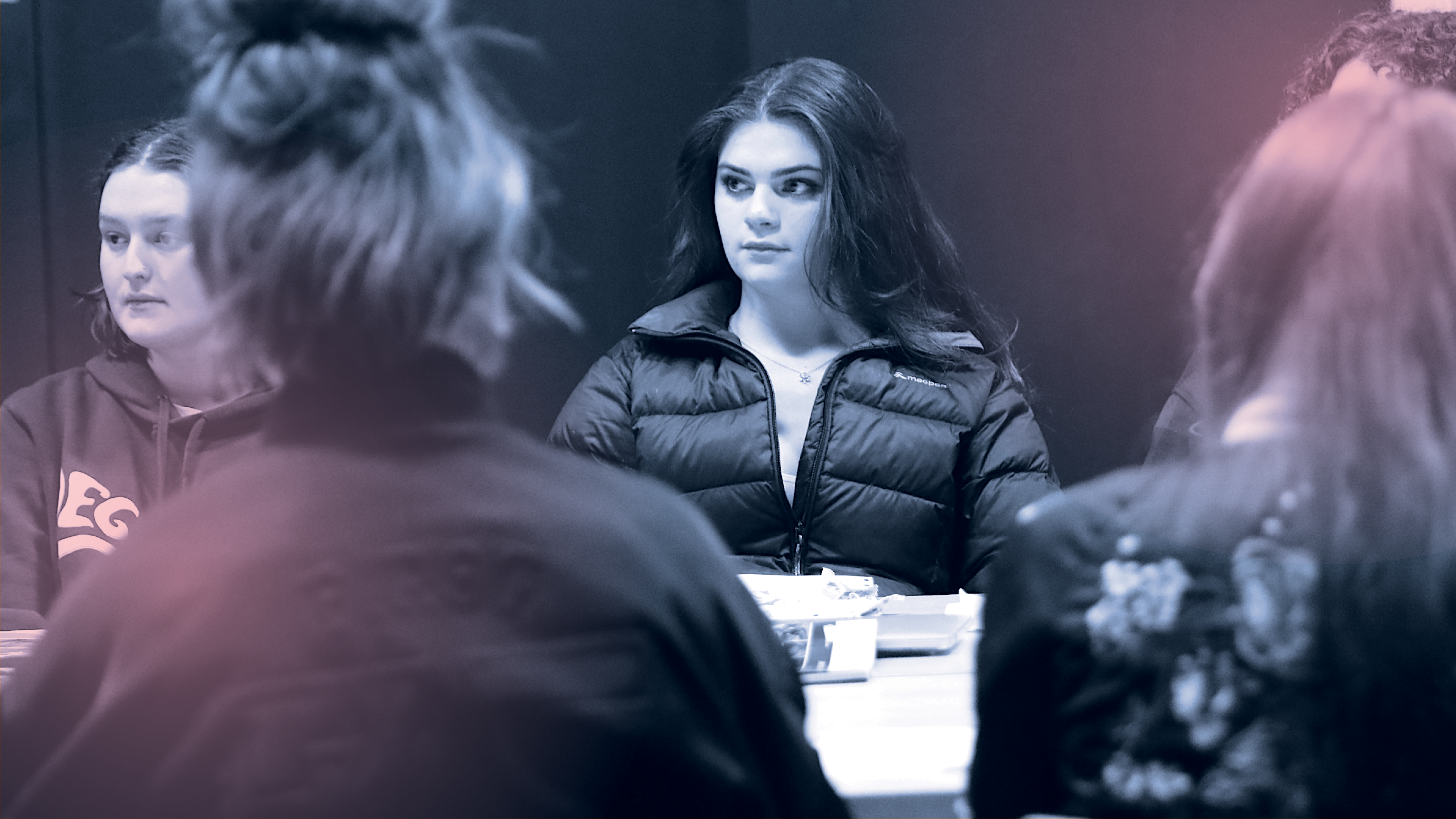 A group of teenagers sit attentively around a table.